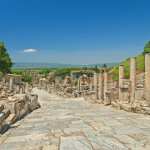 marble alley with columns leading to the Celsus Library in ancient greek city of Ephesus with mountains and clear blue sky at background with single small cloud over the Celsus Library, Turkey