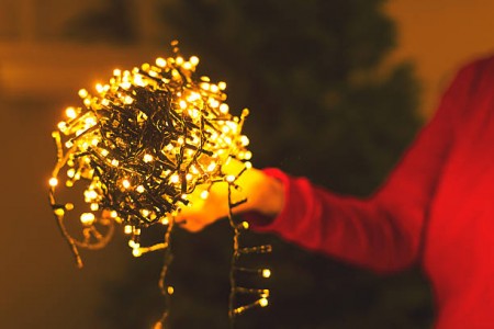 Ball of tangled Christmas lights held up by a lady in front of a Christmas tree